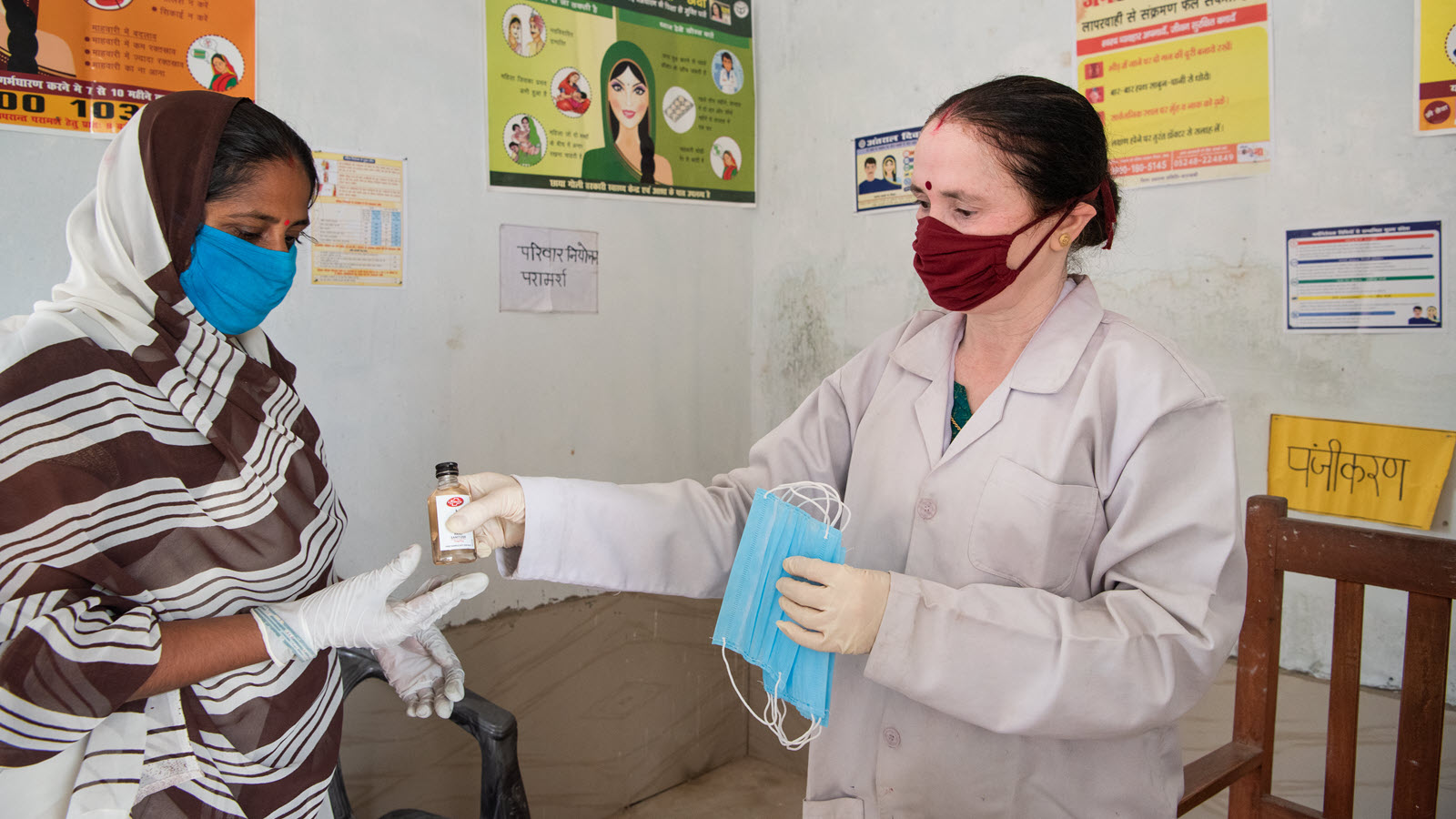 An auxiliary nurse midwife in Uttar Pradesh hands out hand sanitizer and masks.