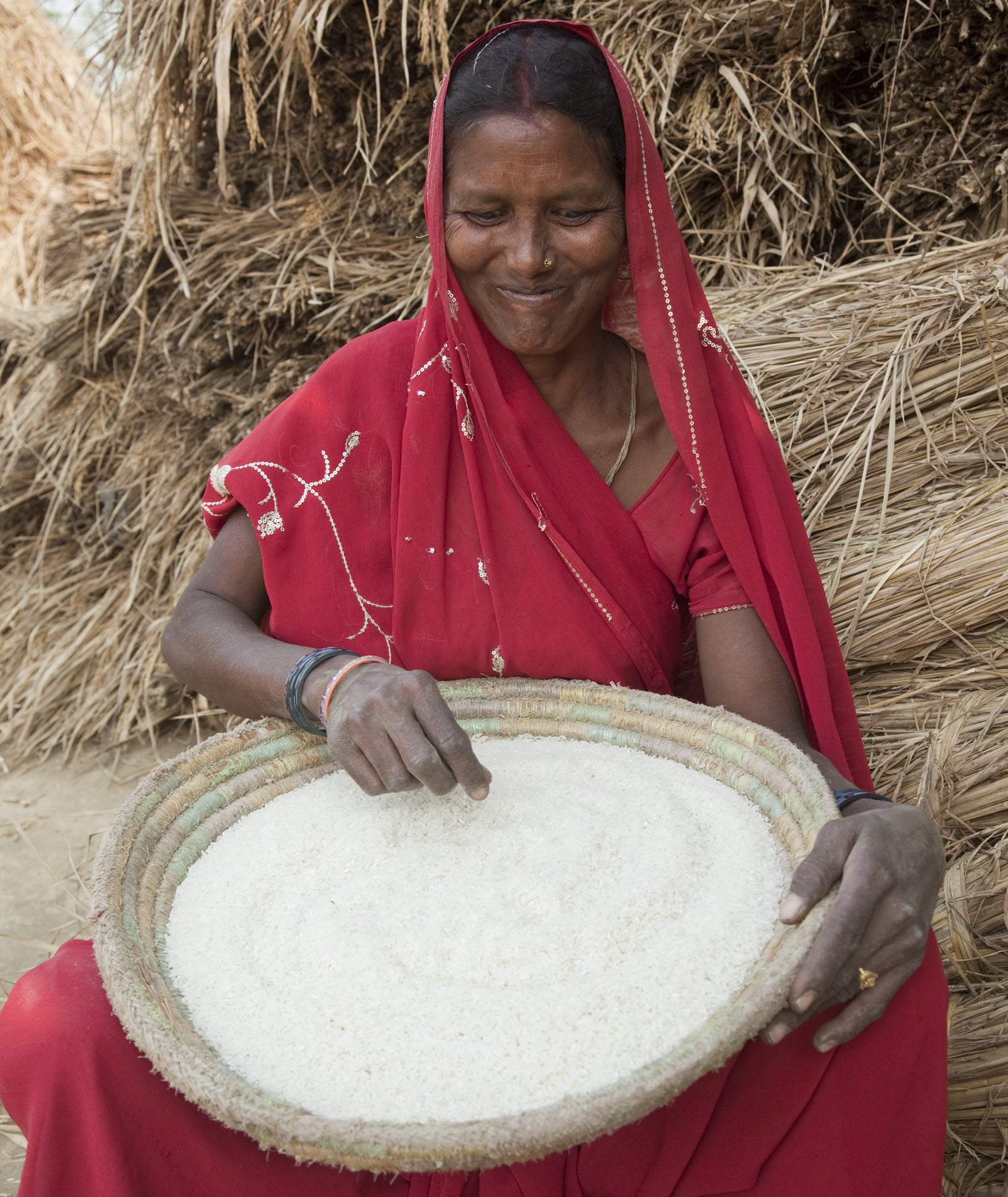 A woman smiles while holding a woven basket of harvested grain.