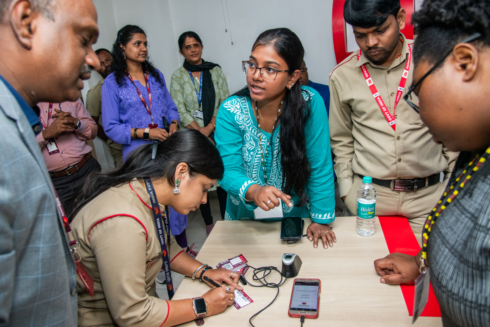 Community members and India Post staff use digital ID tools and a biometric scanner at a service table.